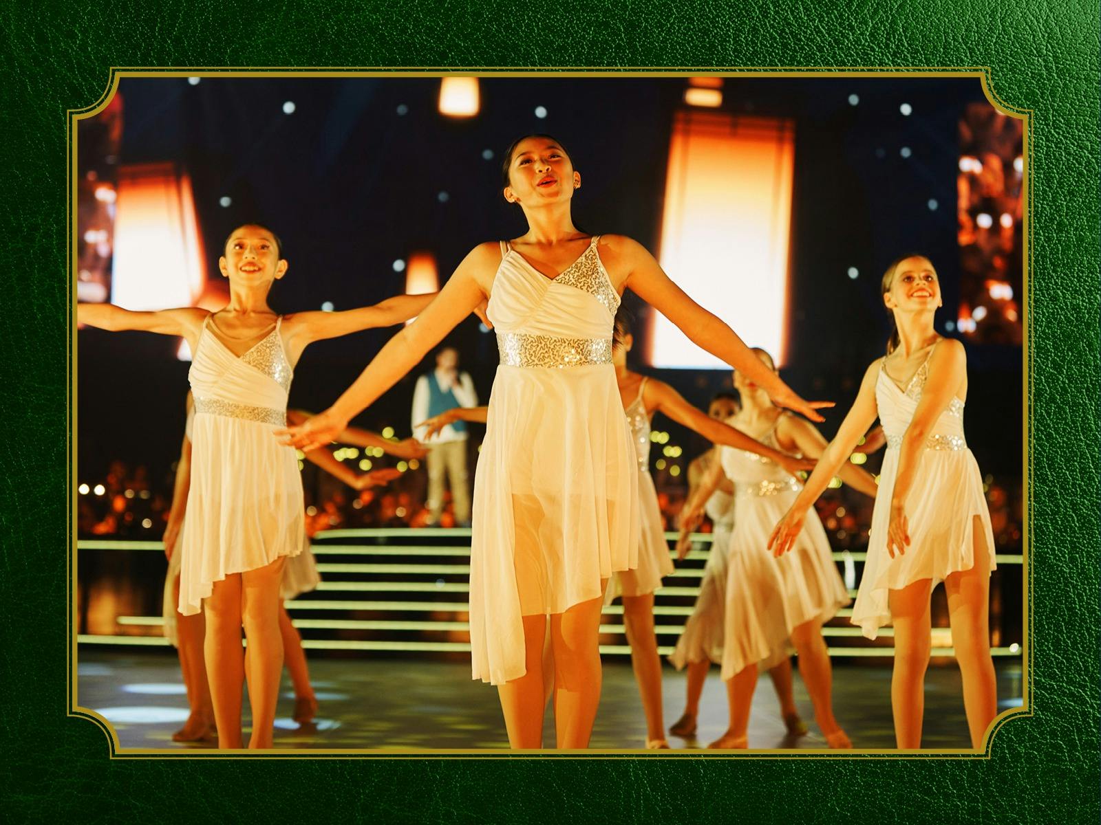 Photo of girls in white dresses dancing on a stage in front of large warm white lanterns