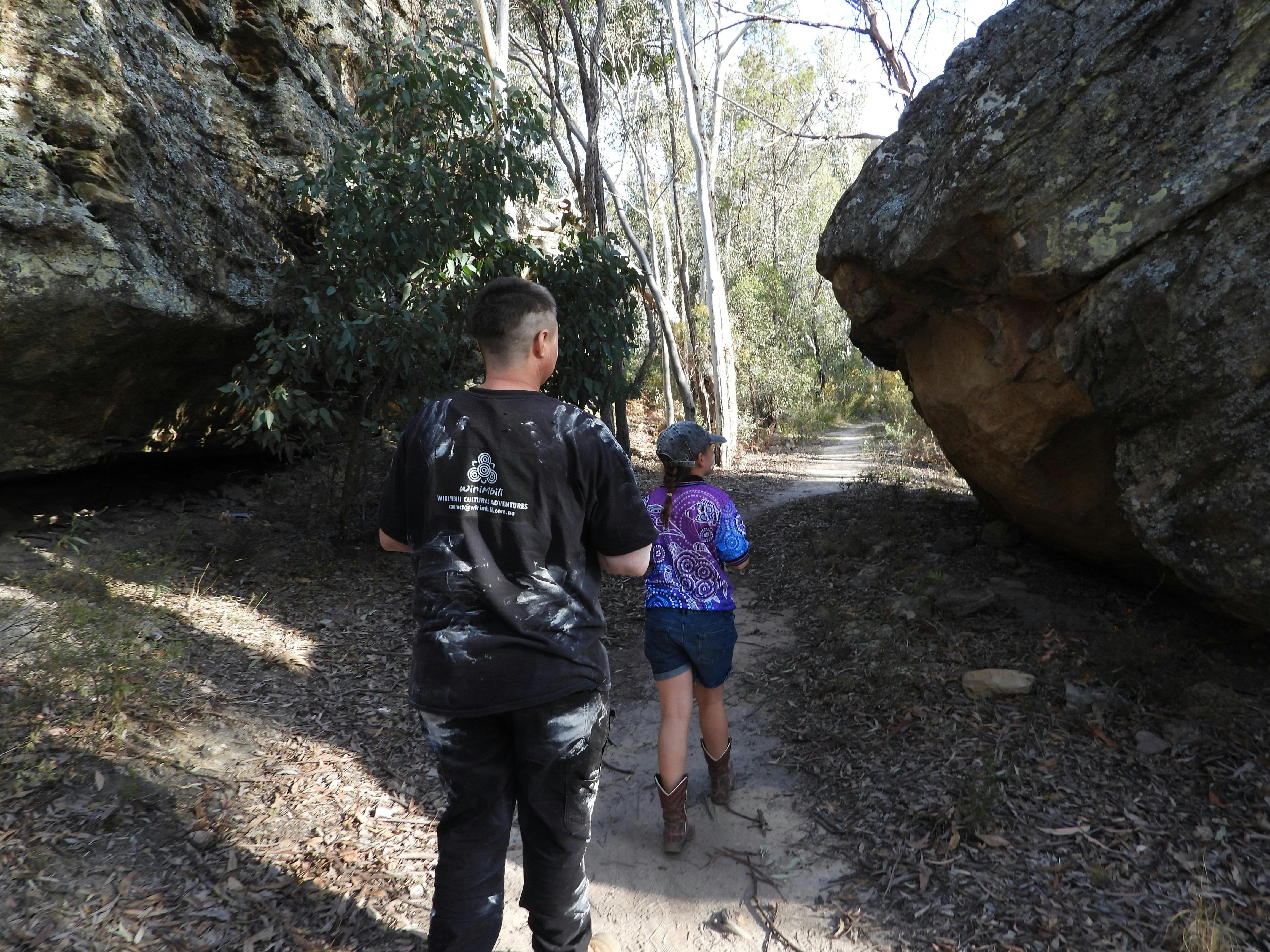 Tour guide and child walk along a flat dirt path between huge rocks
