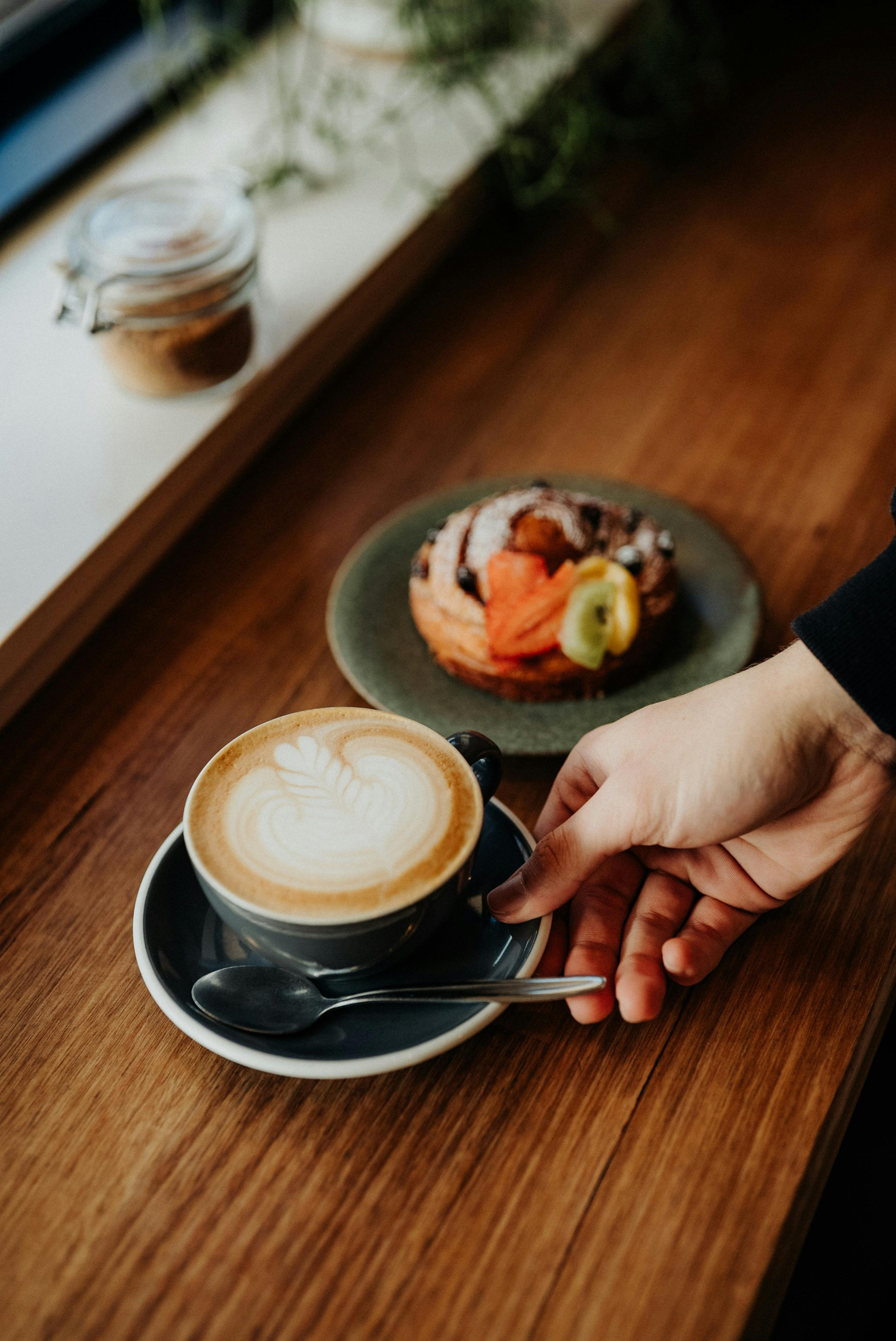 Hand places coffee with beautiful latte art down on table next to fruit covered pastry