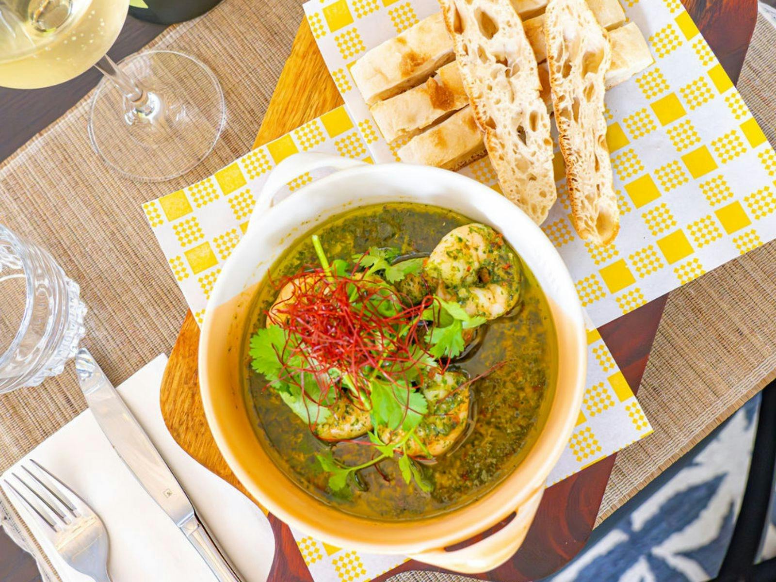 Bowl of prawns with herbs and chili, served with slices of rustic bread on the side.