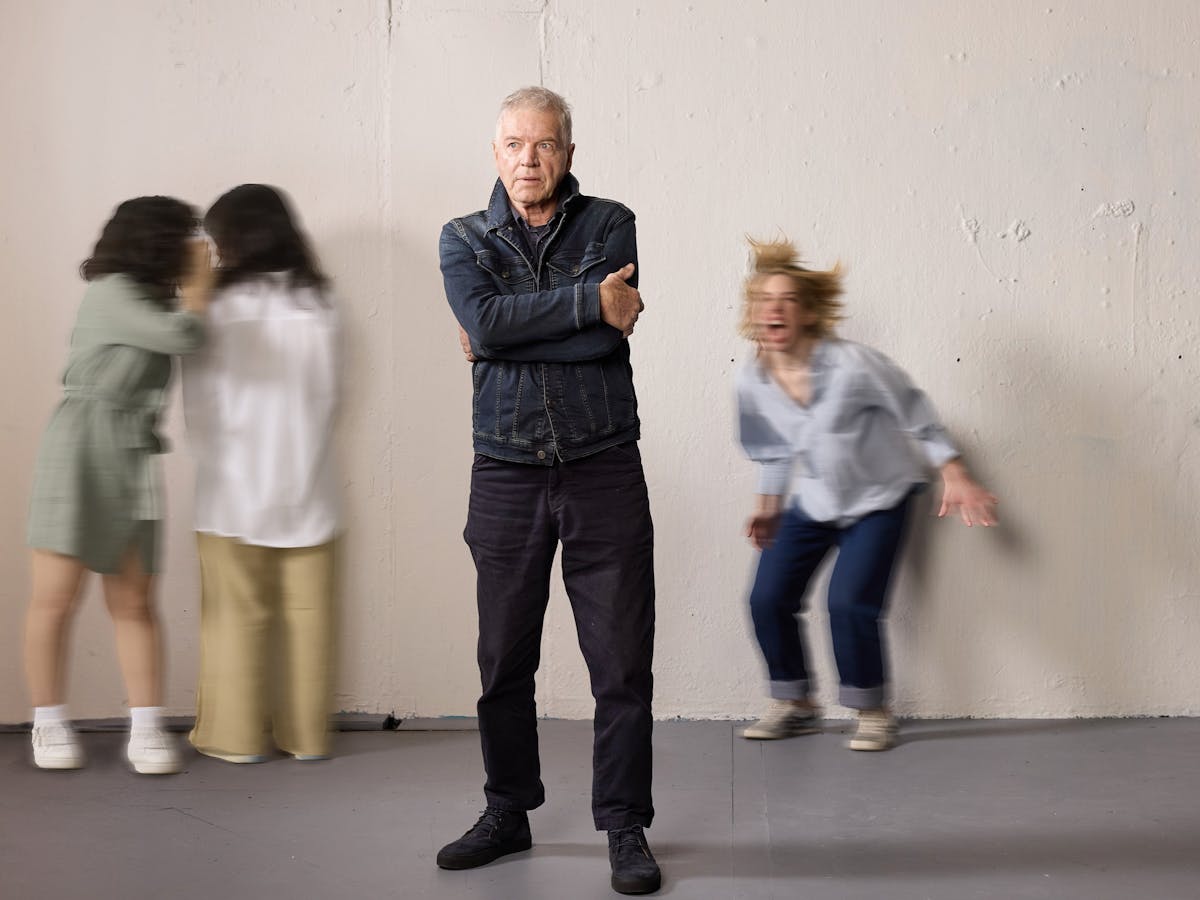 An older man standing with crossed arms with his three daughters in the background