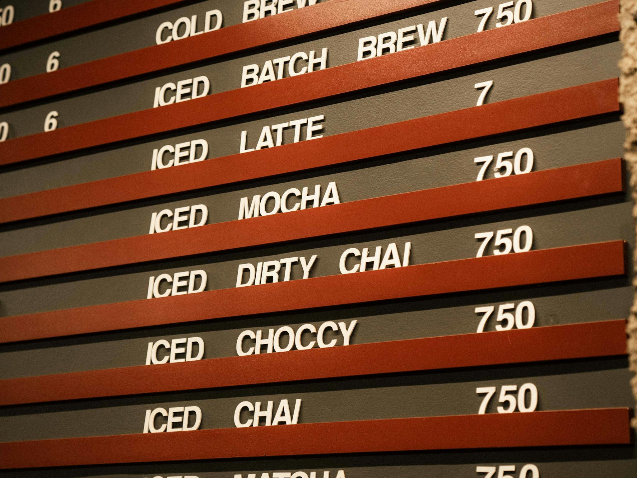 A photo of one half of a menu board that is in capitalised font in white it is the iced drinks menu A photo of one half of a menu board that is in capitalised font in white it is the iced drinks menu
