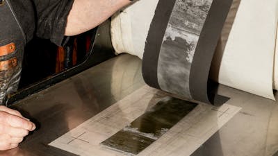 A photograph of hands peeling a print off of a press