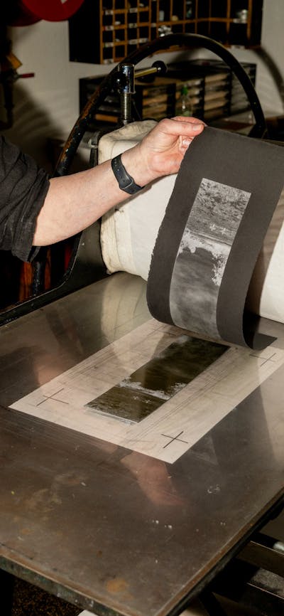 A photograph of hands peeling a print off of a press