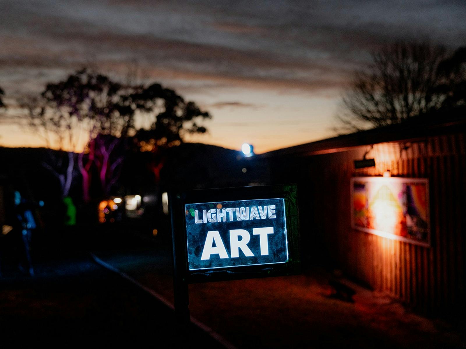 An illuminated ART sign in front of a building lit with coloured light.
