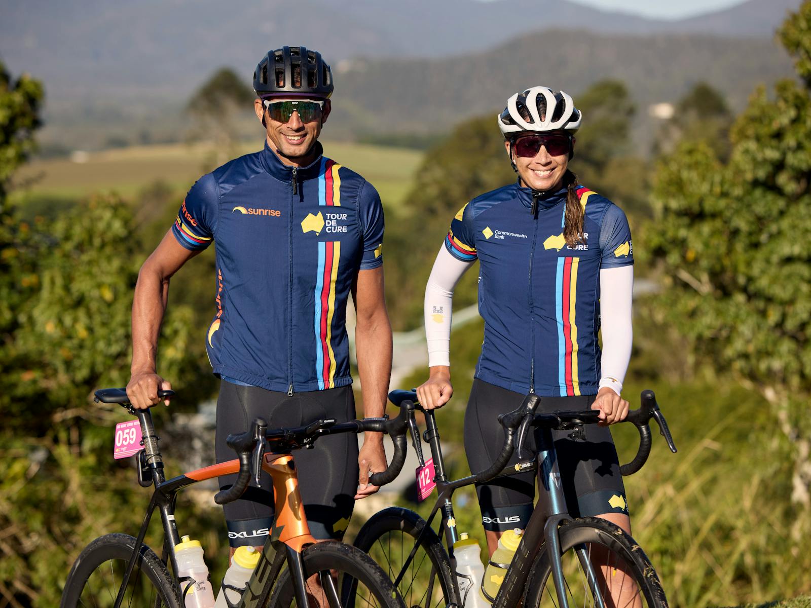 Male and female cyclist standing in scenic background smiling at the camera off-bikes