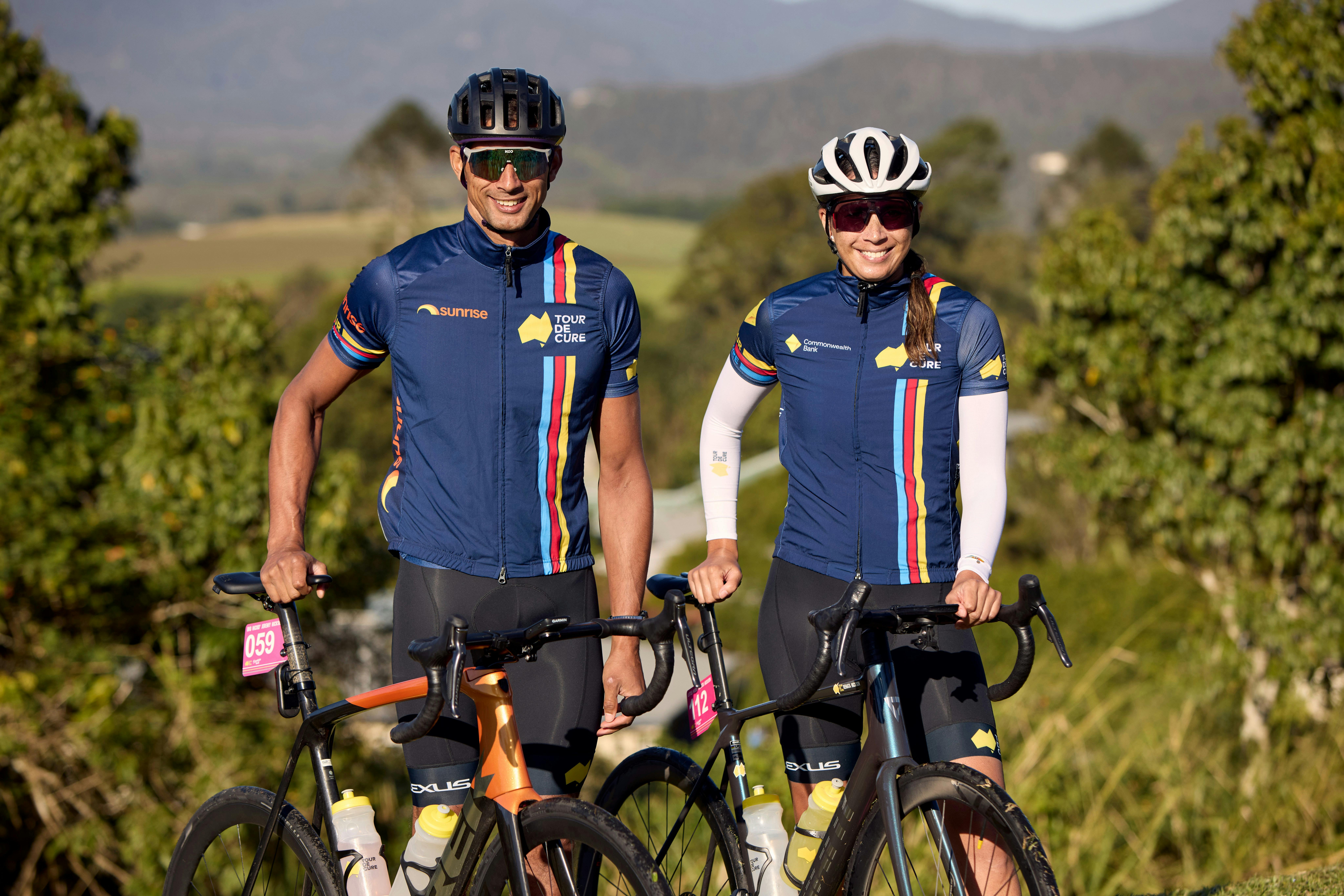 Male and female cyclist standing in scenic background smiling at the camera off-bikes