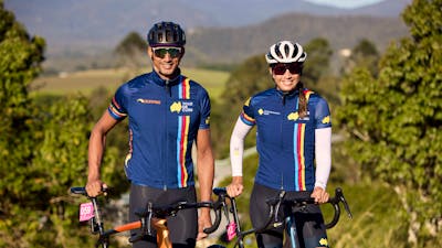 Male and female cyclist standing in scenic background smiling at the camera off-bikes