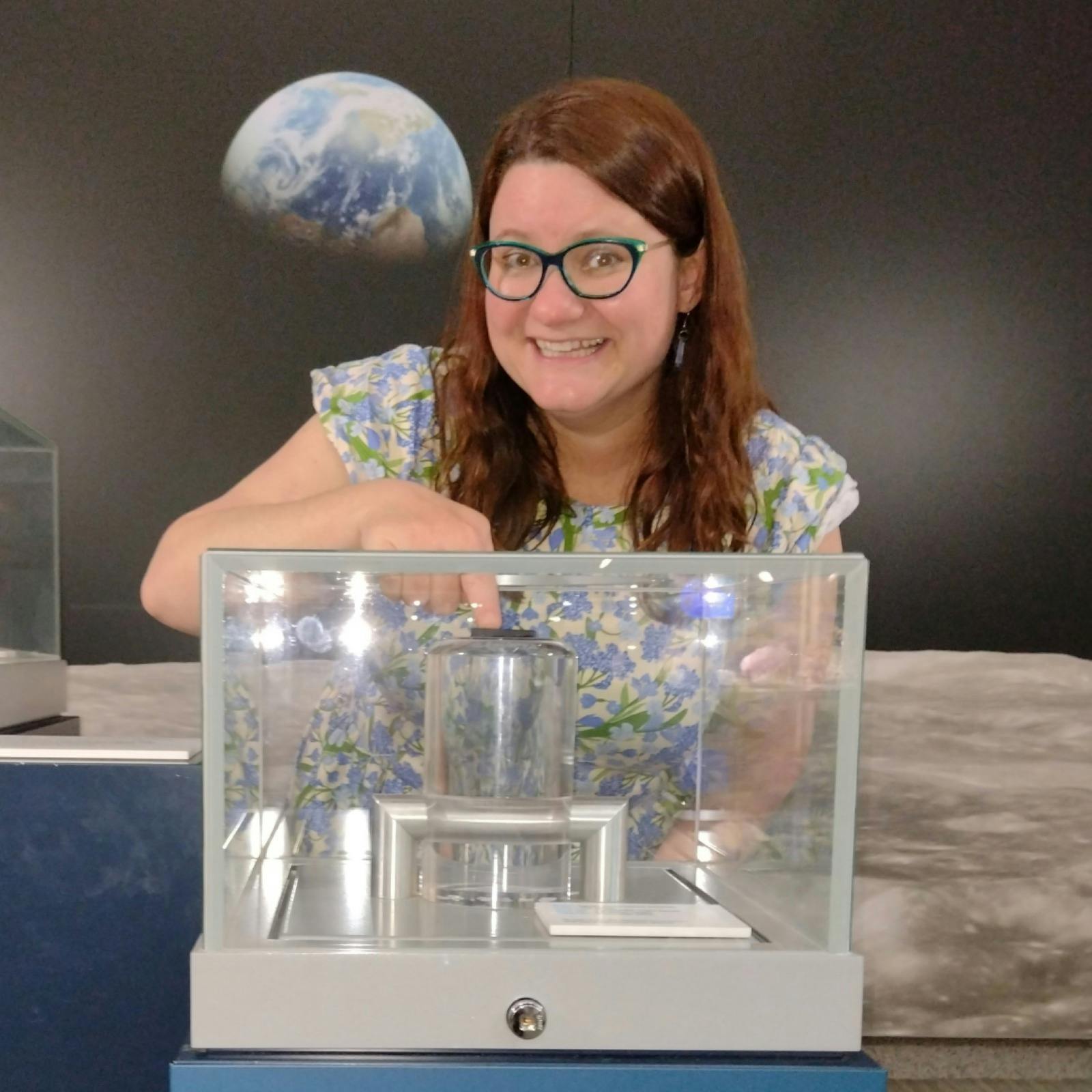 A woman touches a small rock  in a cabinet with an image of the Moon and Earth behind her.
