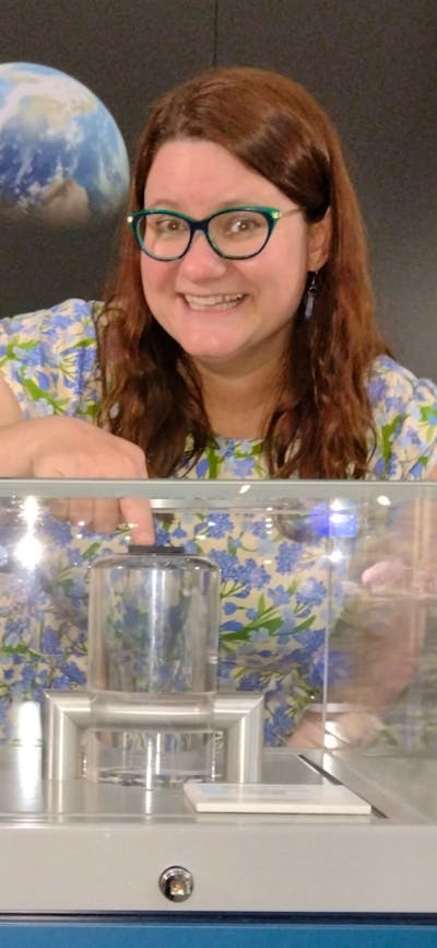 A woman touches a small rock in a cabinet with an image of the Moon and Earth behind her.