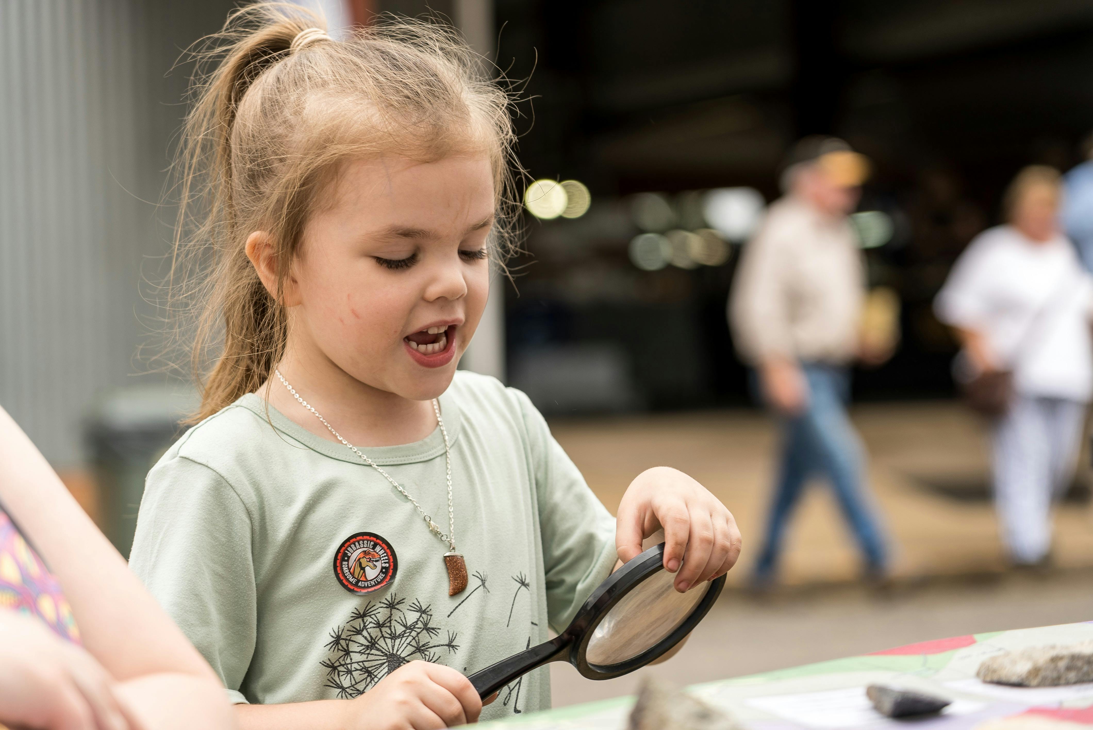 Young girl with magnifying glass at UNE Discovery Voyager marquee at Minerama
