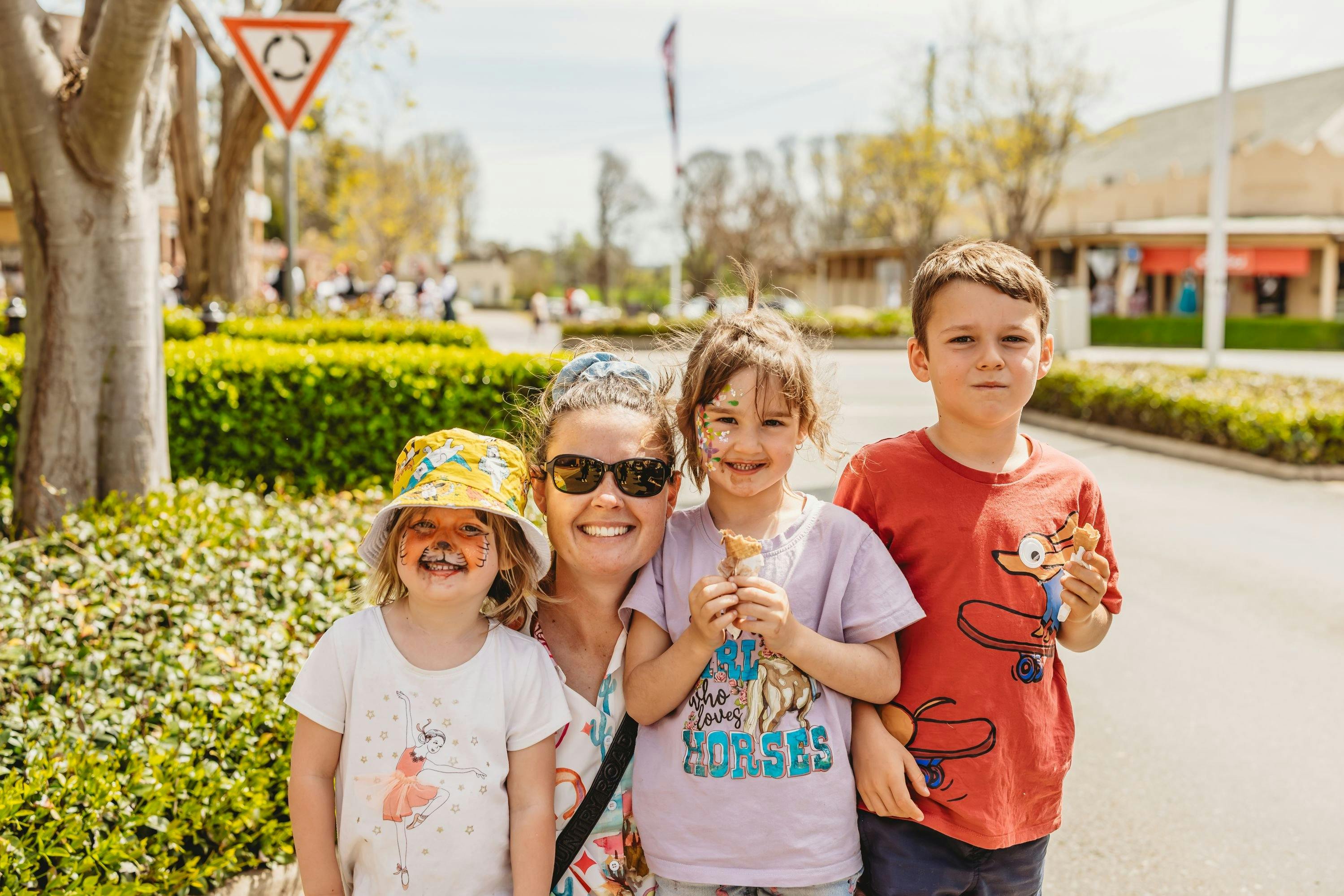Mother with 3 of her children eating ice cream. Two of the children have their faces painted.