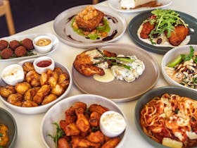 A table spread of pub meals including pasta, chicken schnitzel, arancini and wedges