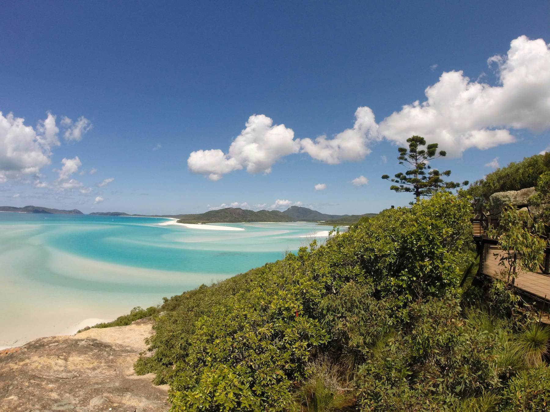 Boardwalk along the hill with turquoise water and swirling sand in the backrgound