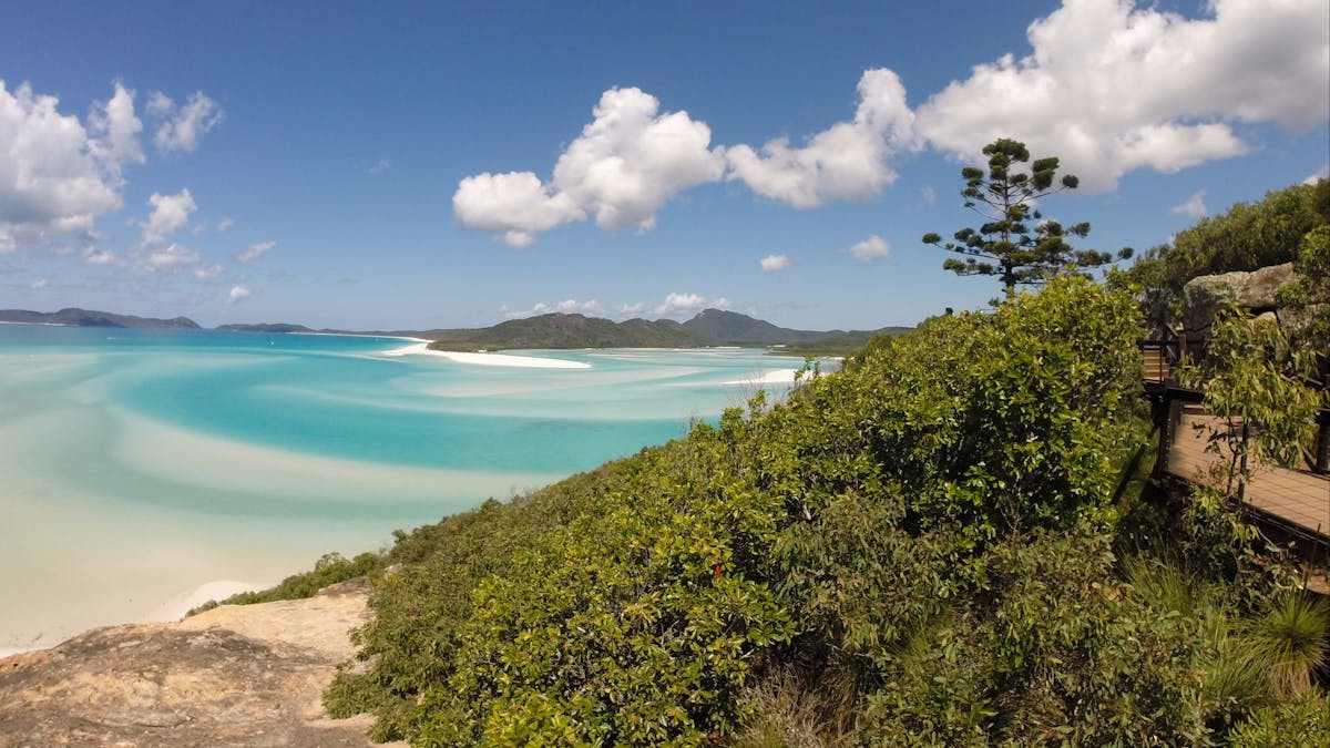 Boardwalk along the hill with turquoise water and swirling sand in the backrgound