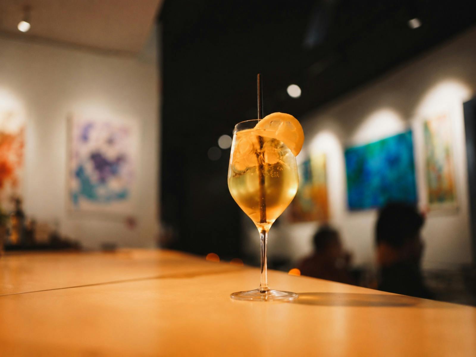An image of an aperol spritz on the bar with art in the background.