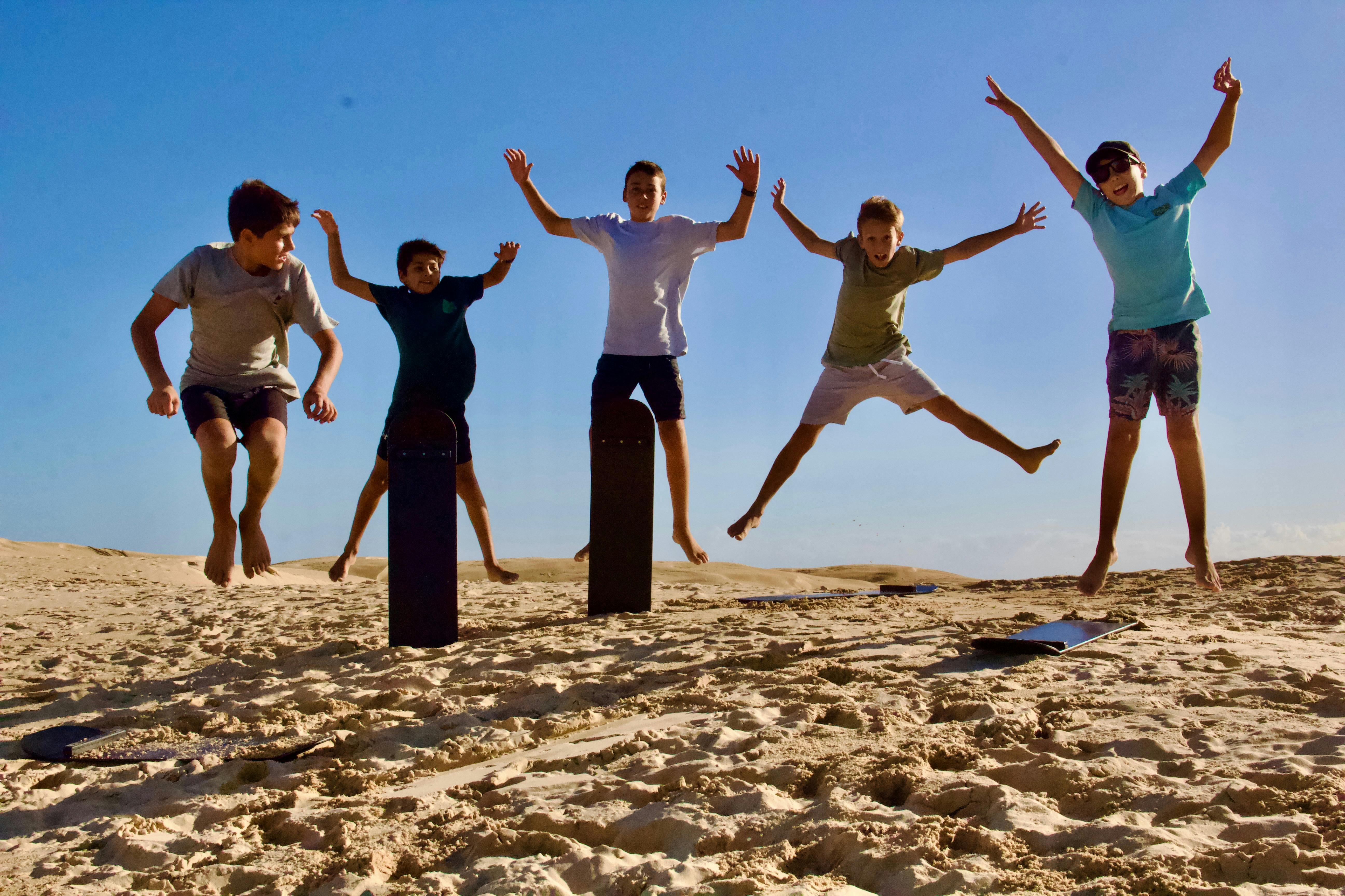 5 kids jumping in the air after sliding dow the sand dune
