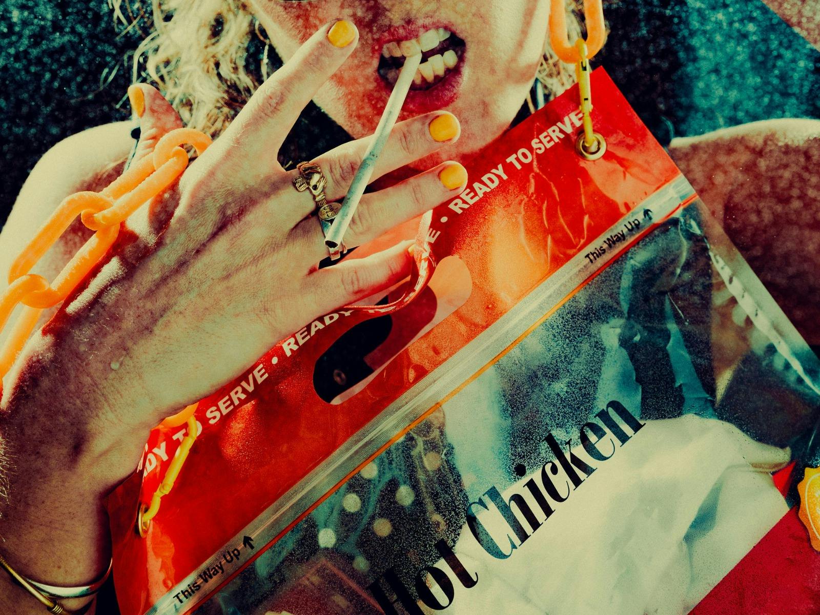 a close up of a hot chicken bag with a hand about to pinch a cigarette with two fingers