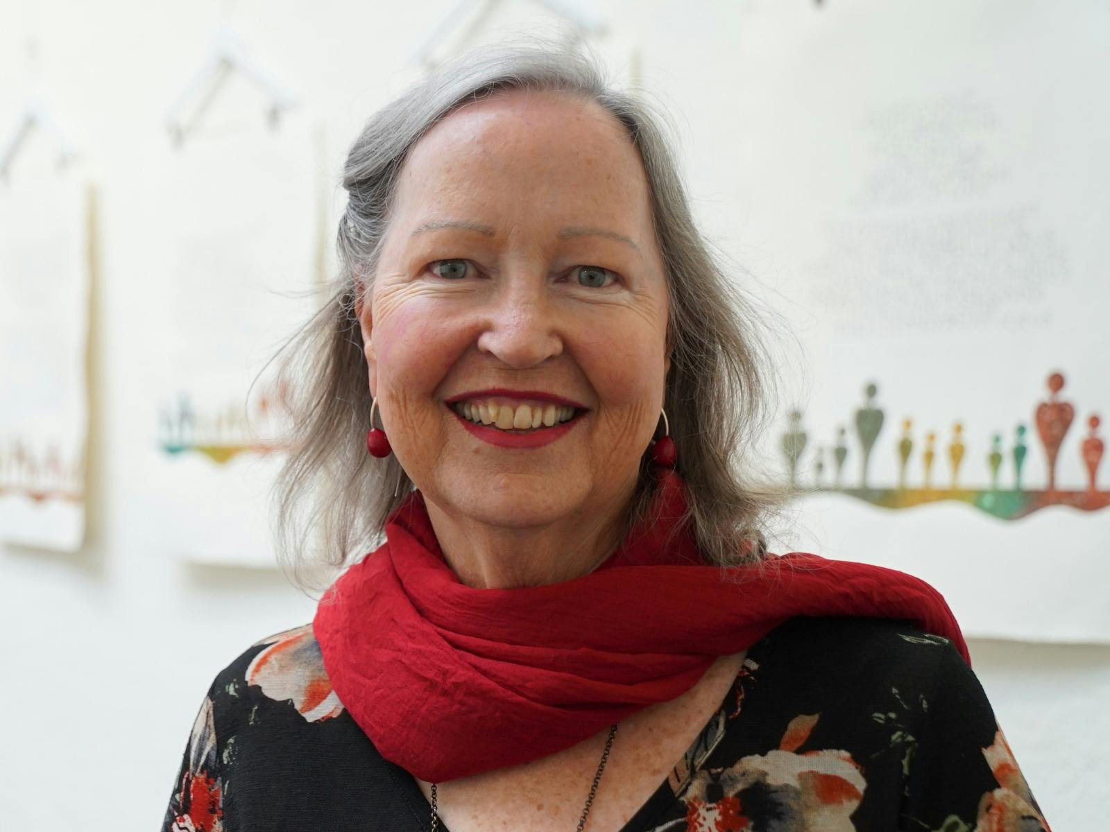 A smiling woman with gray hair wearing a red scarf over a dark floral top.