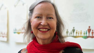 A smiling woman with gray hair wearing a red scarf over a dark floral top.