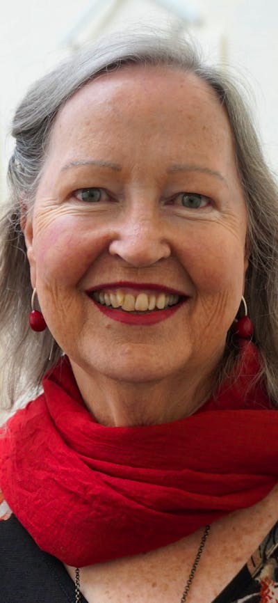 A smiling woman with gray hair wearing a red scarf over a dark floral top.