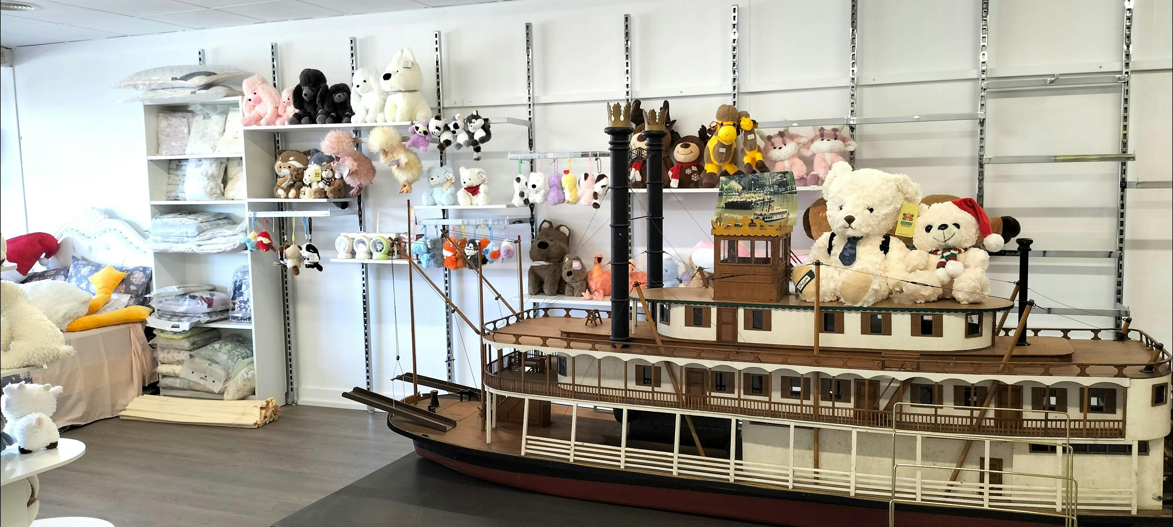 貨架上擺滿了可愛的動物毛絨玩具和包包掛飾，商店的中心擺放著一艘大型模型船。