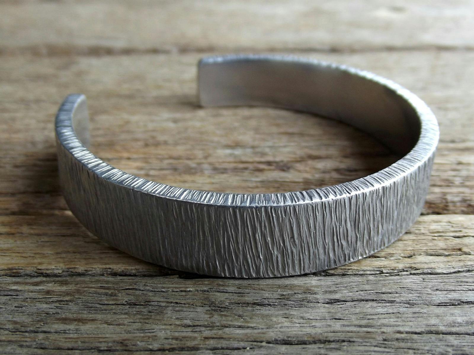 Silver-smithed bracelet with textured pattern displayed on wooden bench. Silver-smithed bracelet with textured pattern displayed on wooden bench.