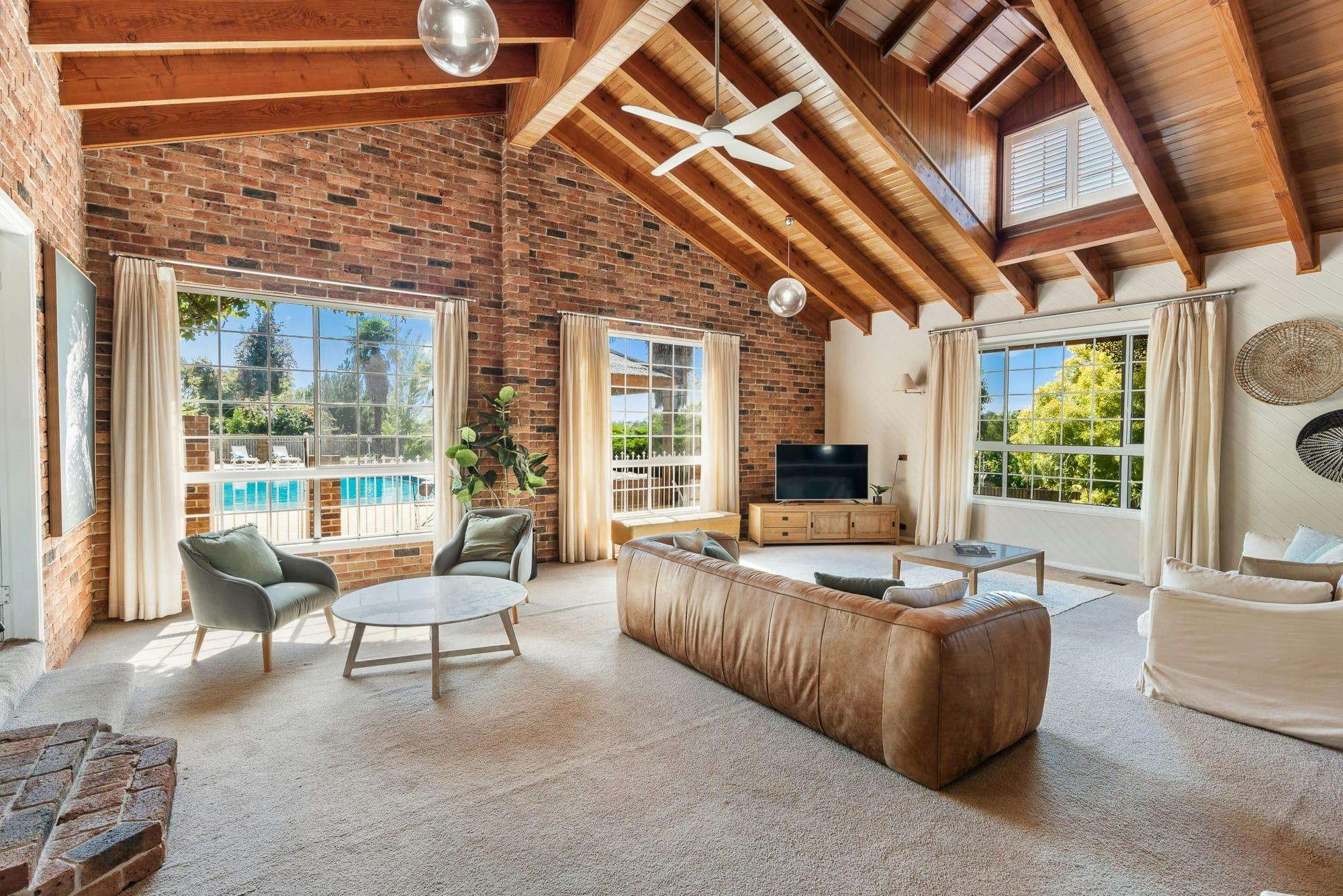 Large open living room with brown leather couch, open windows to outside with the pool