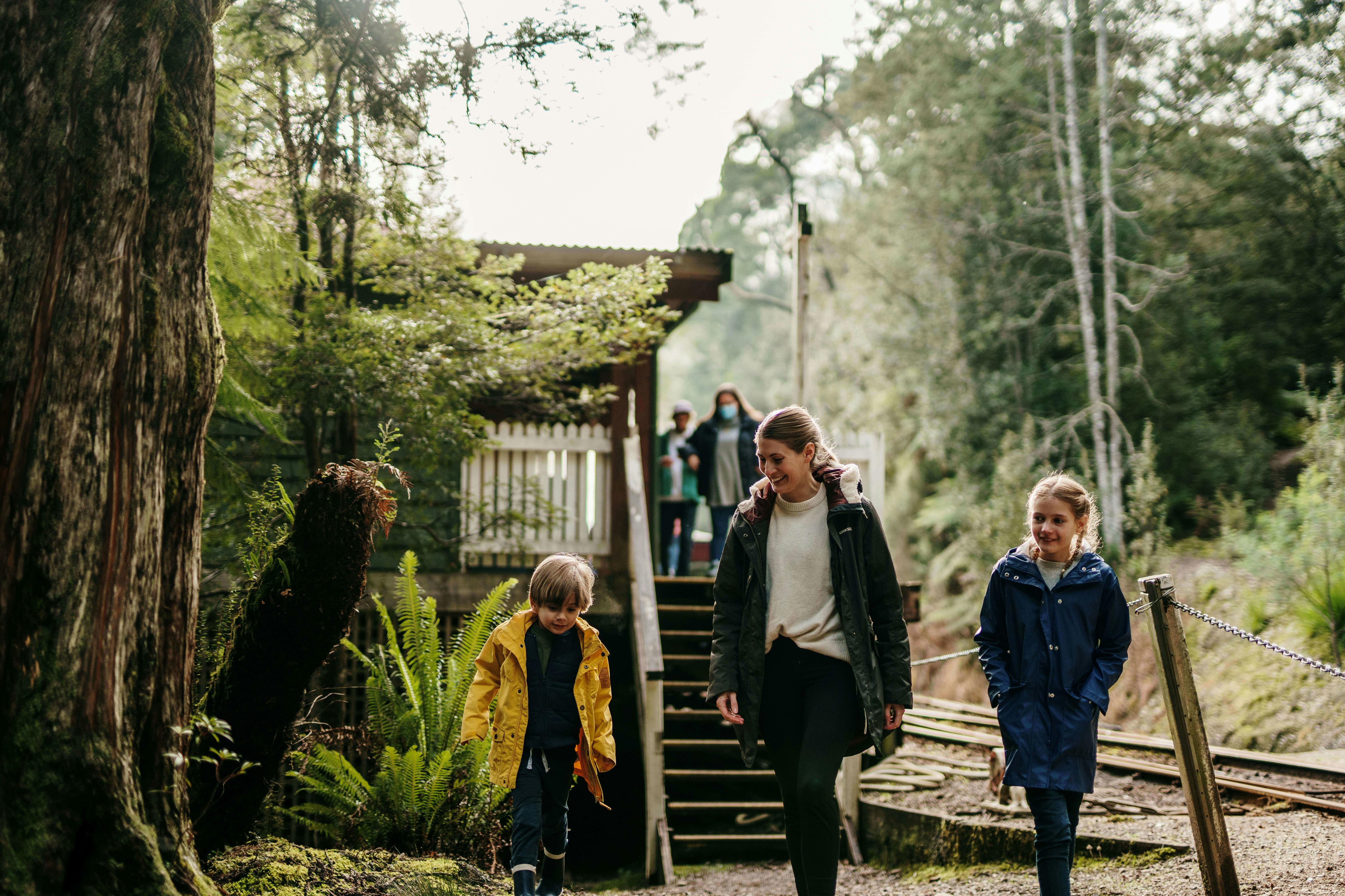 A mother and two young children walk away from a train platform built in the rainforest