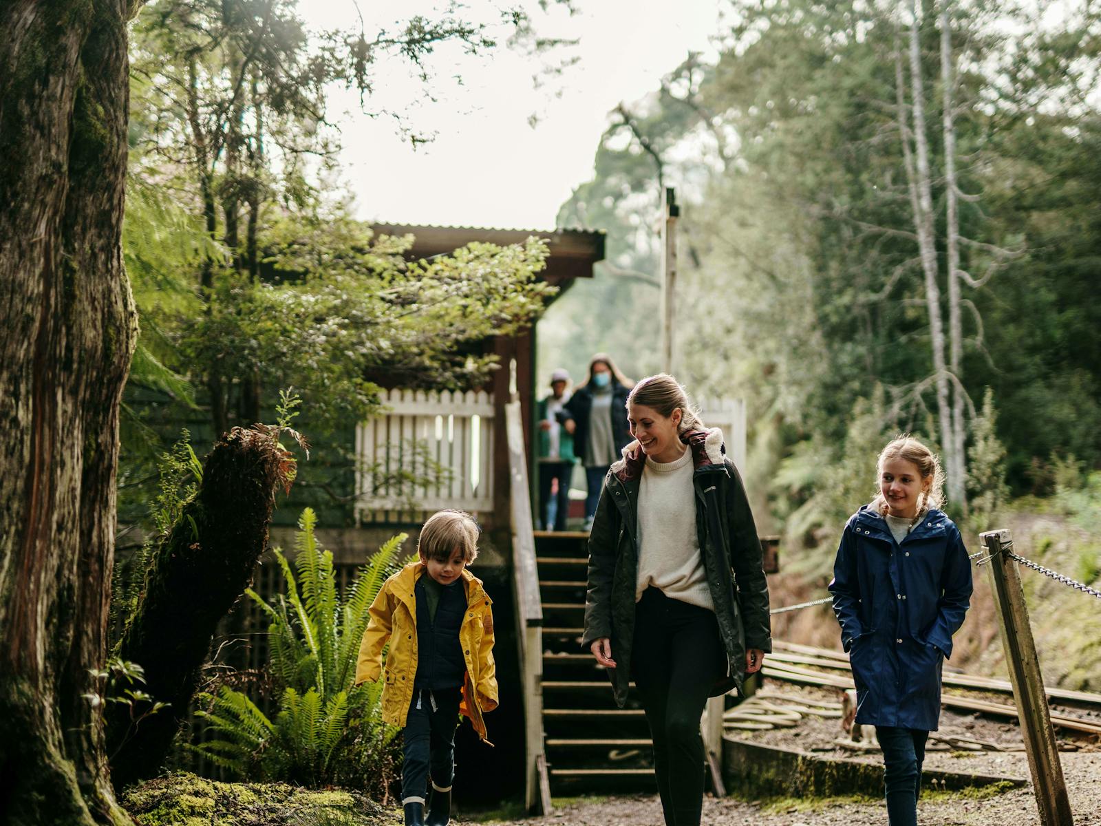 A mother and two young children walk away from a train platform built in the rainforest