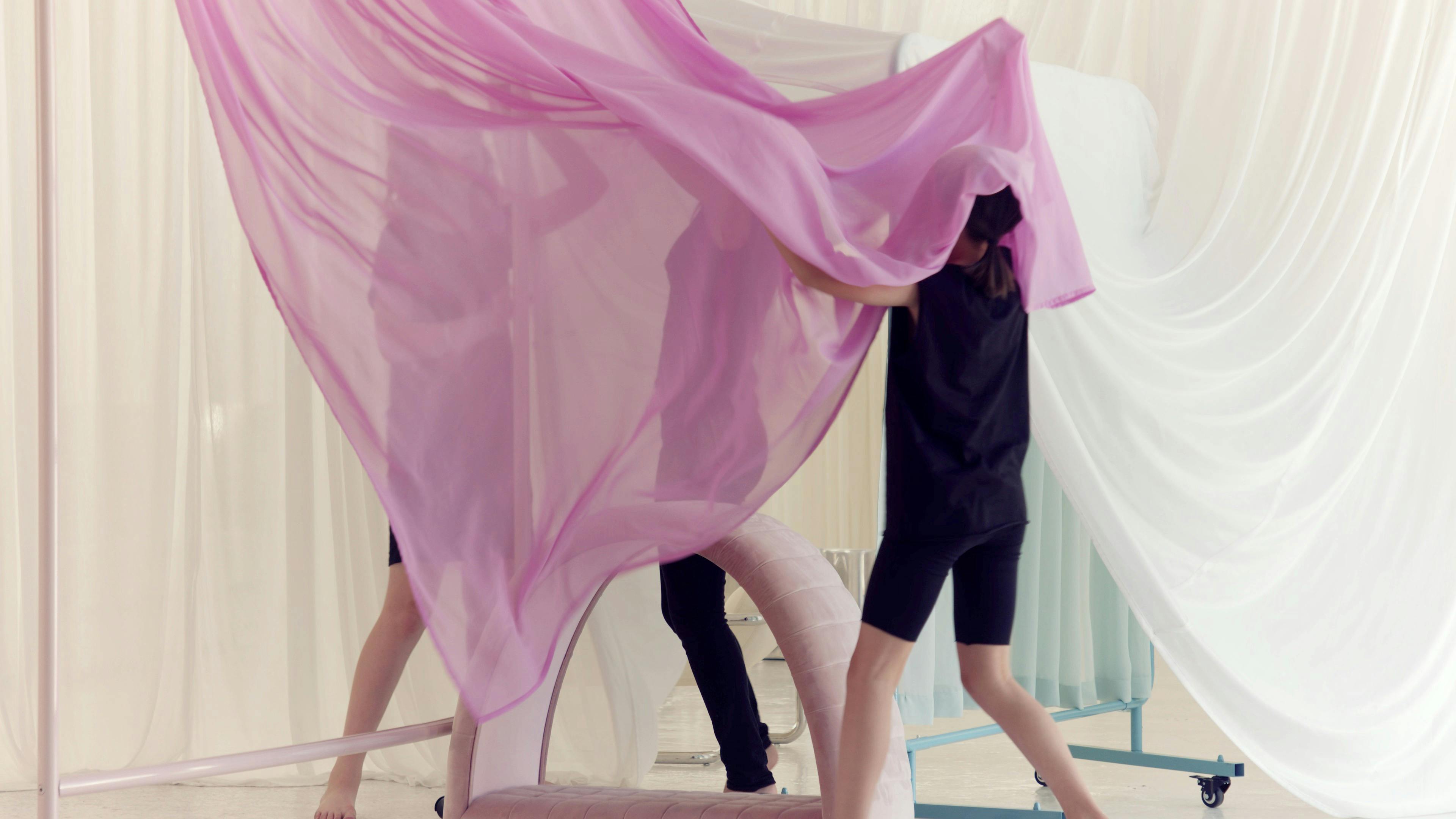 Three friends dressed in black play amongst pastel-coloured silk chiffon curtains