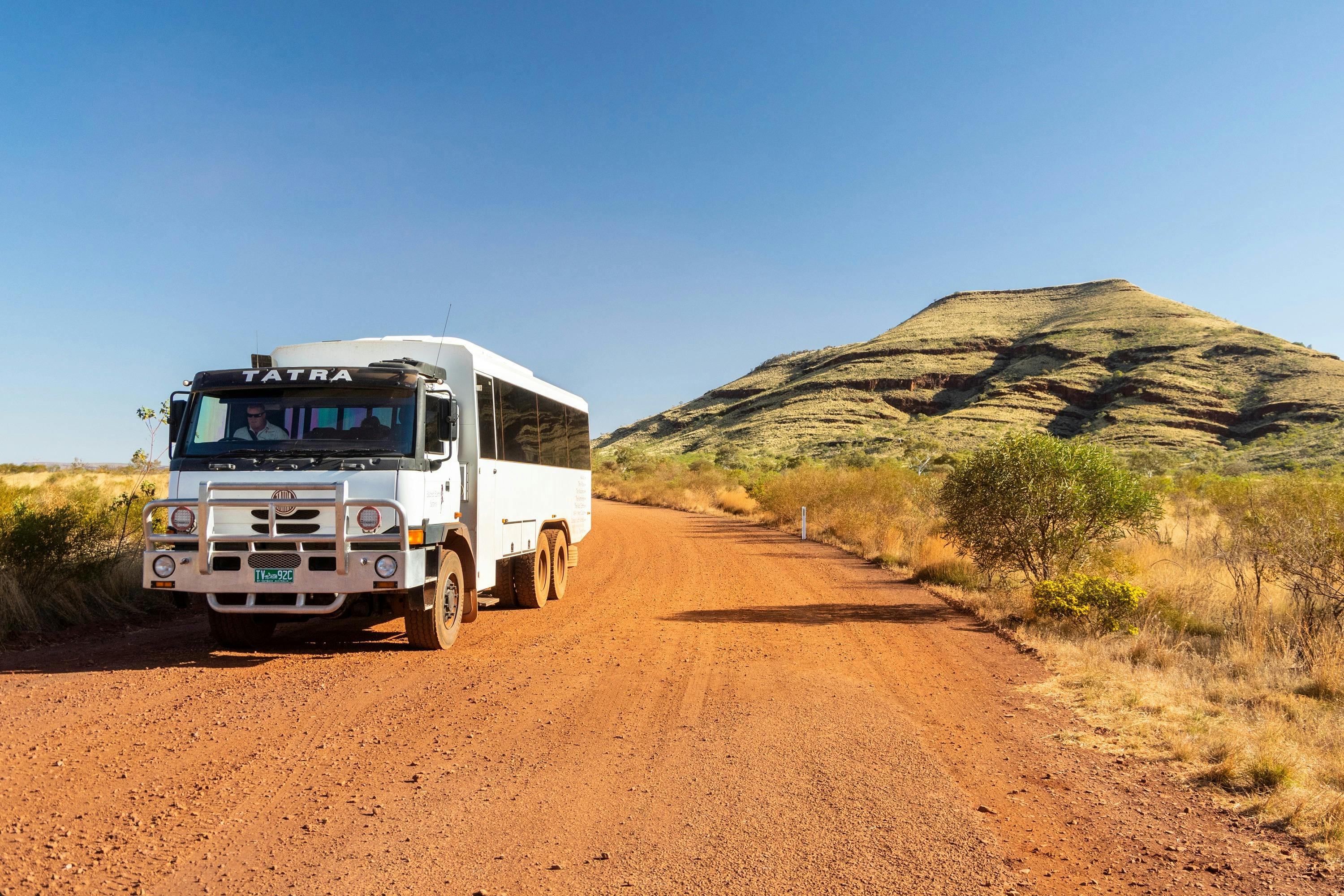 6WD tour coach on a red dirt road and small hill in background
