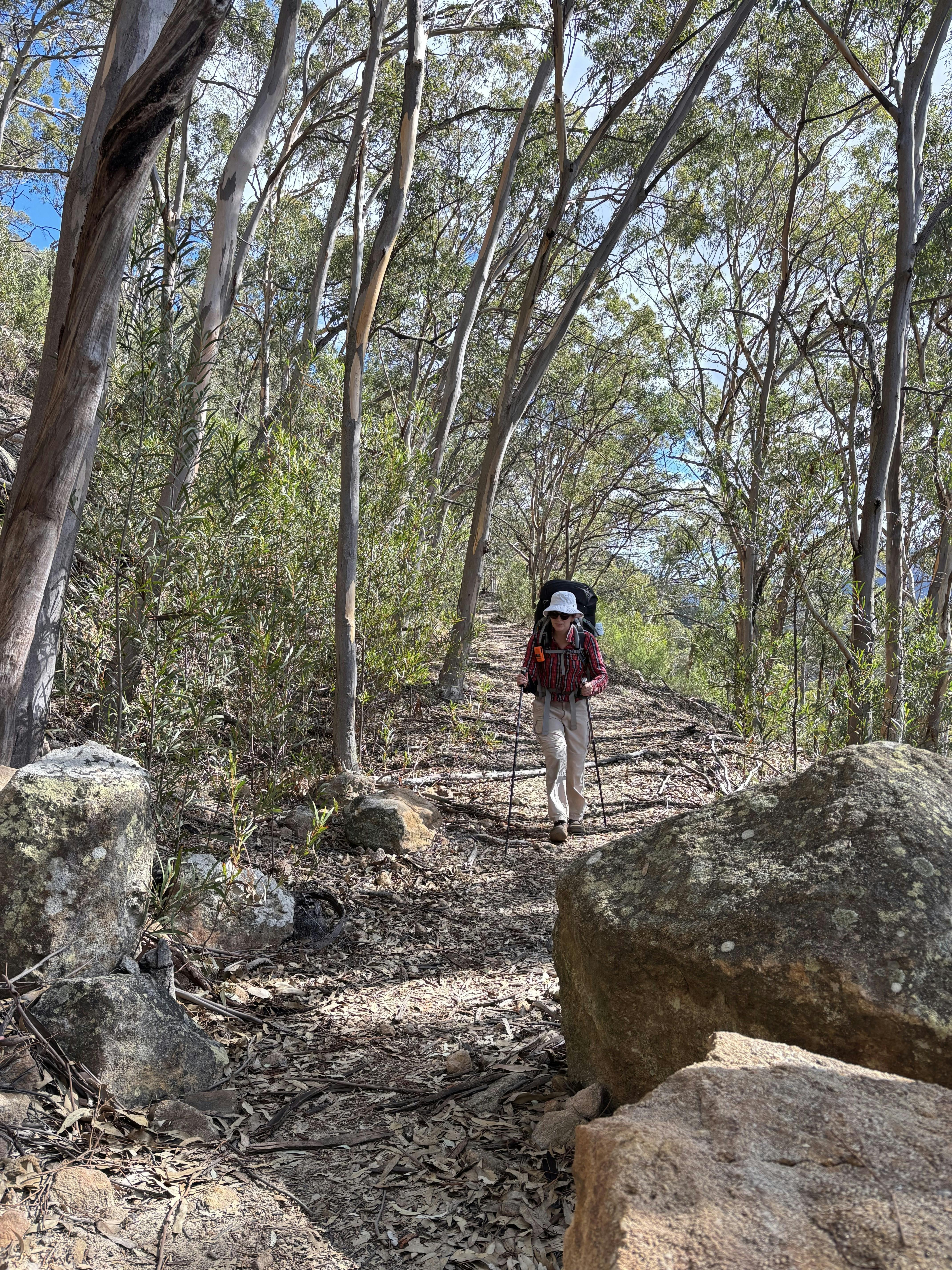 A woman wearing a red checked shirt and backpack walking along the former Wolgan Valley Railway.