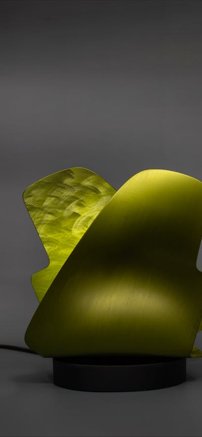 A lamp made from a thin sheet of folded burnished metal in an abstract shape.