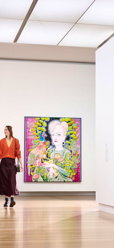 A couple is walking happily through a brightly lit gallery featuring several large portraits.