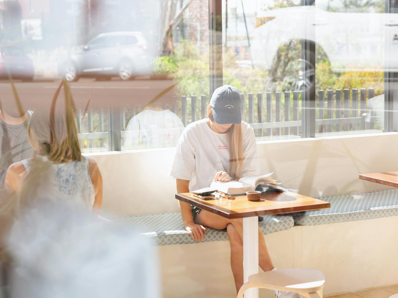 A woman reads a book in the sunshine at a table inside Abercrombie Coffee.