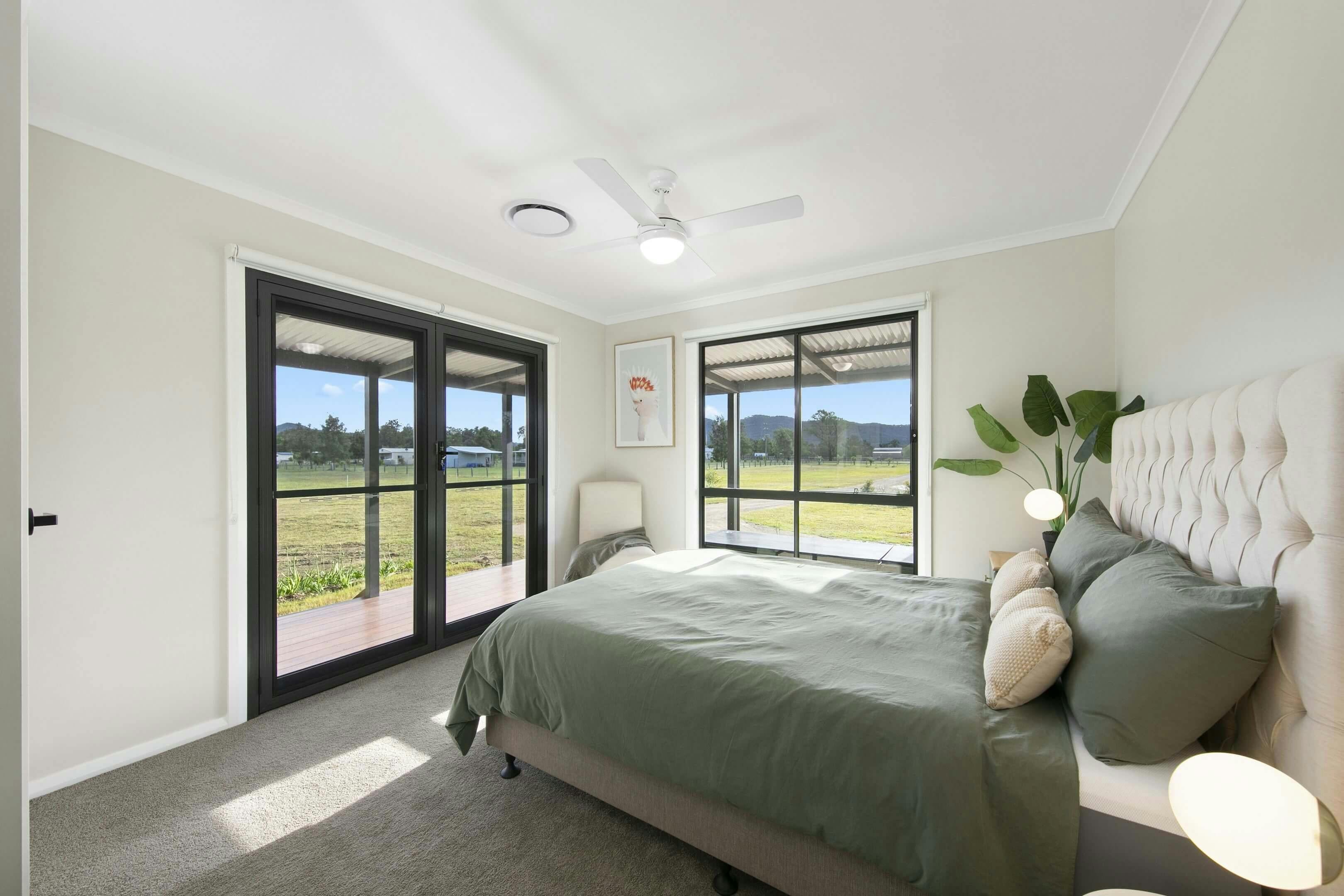 bedroom with a large bed, green bedding, beige headboard, two windows, a glass door to a patio,