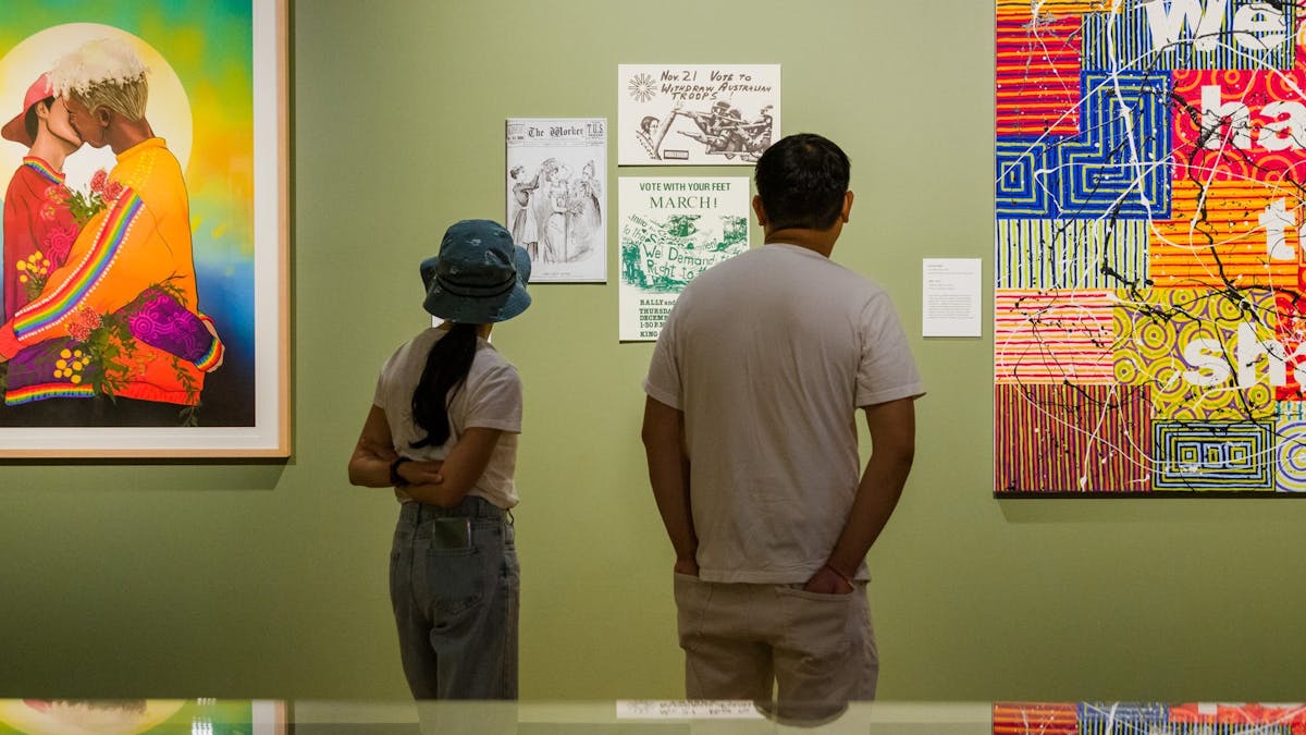 Two people stand in a green-walled gallery space with paintings on the walls. Two people stand in a green-walled gallery space with paintings on the walls.