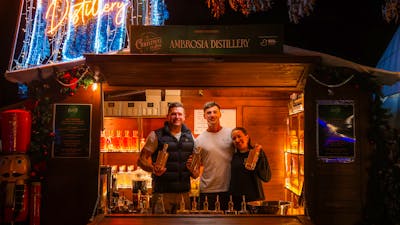 Exhibitors standing in their wooden chalet decorated with Christmas lights, selling liquor