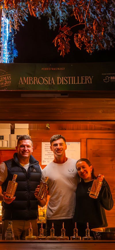 Exhibitors standing in their wooden chalet decorated with Christmas lights, selling liquor