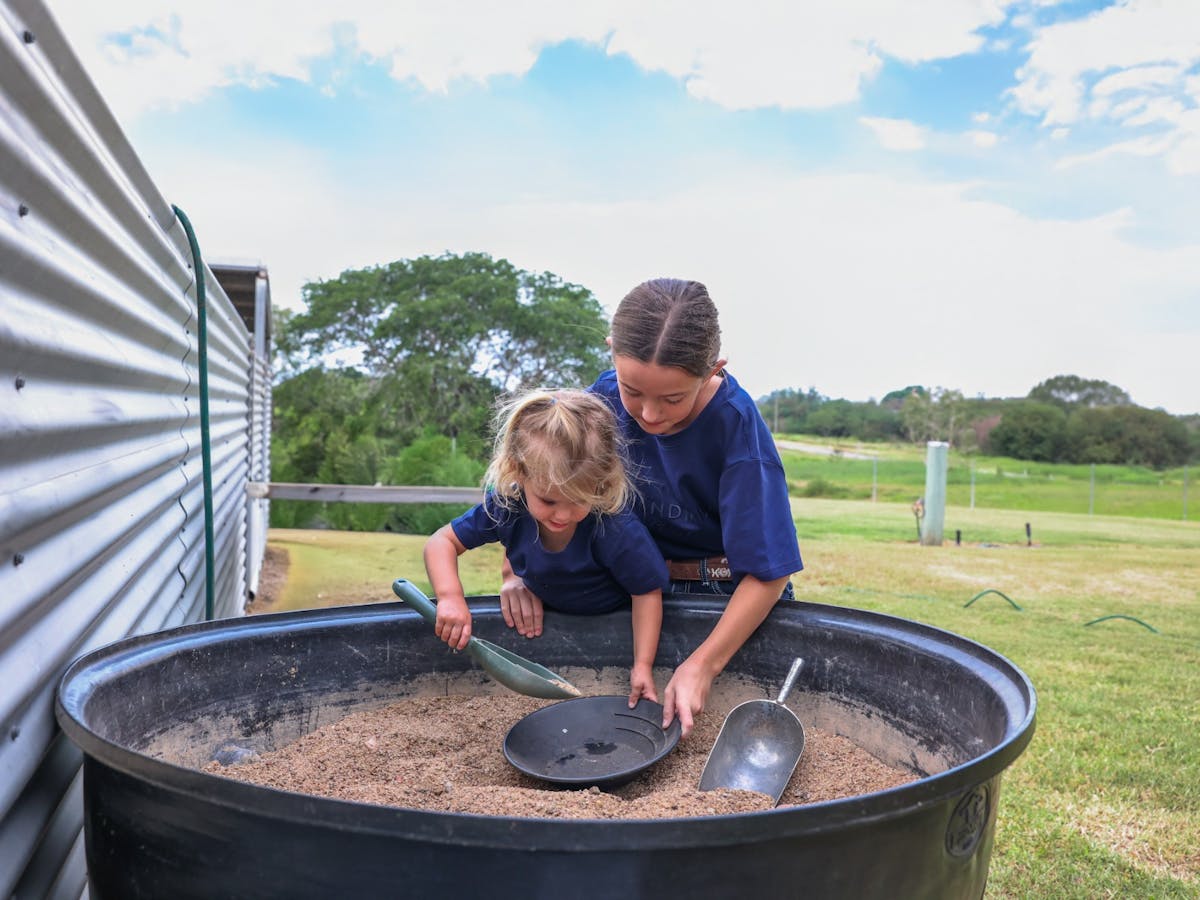 Two kids putting sand into a pan