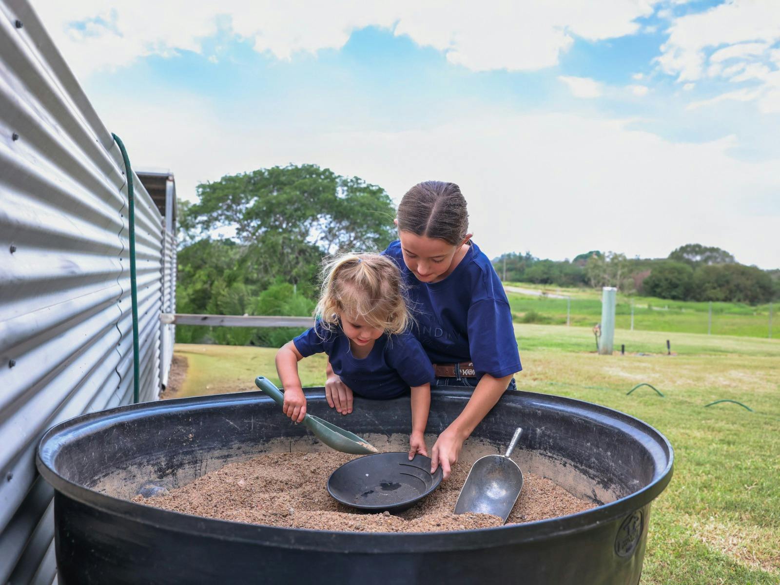 Two kids putting sand into a pan