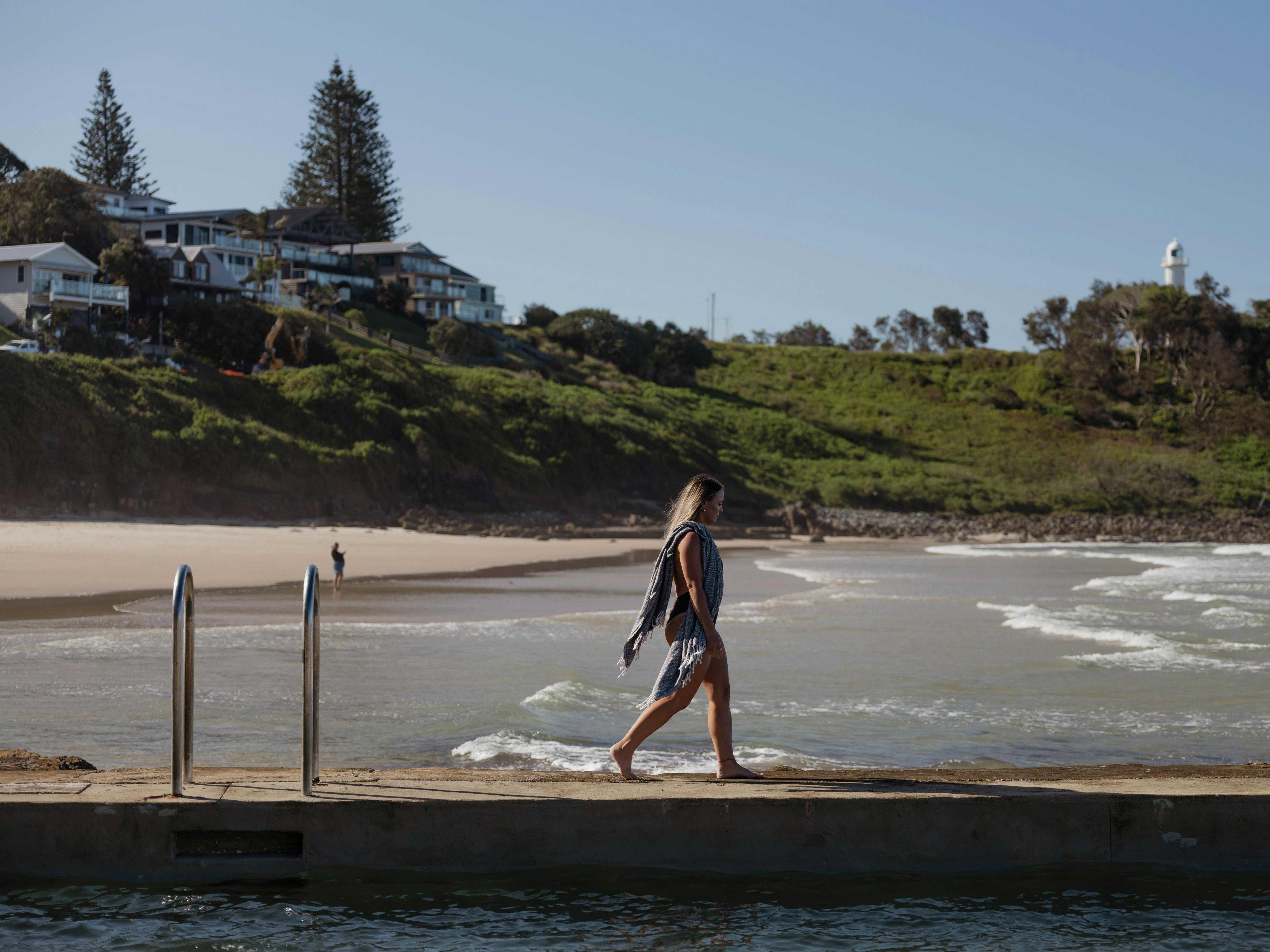 Female in swimsuit with towel walking along ocean baths edge at Yamba Main Beach