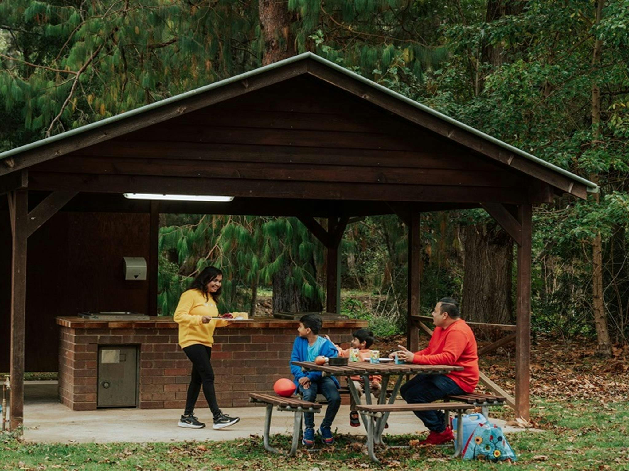 A mother brings dinner to her 2 young sons and husband from the barbecue area at Wombeyan Caves