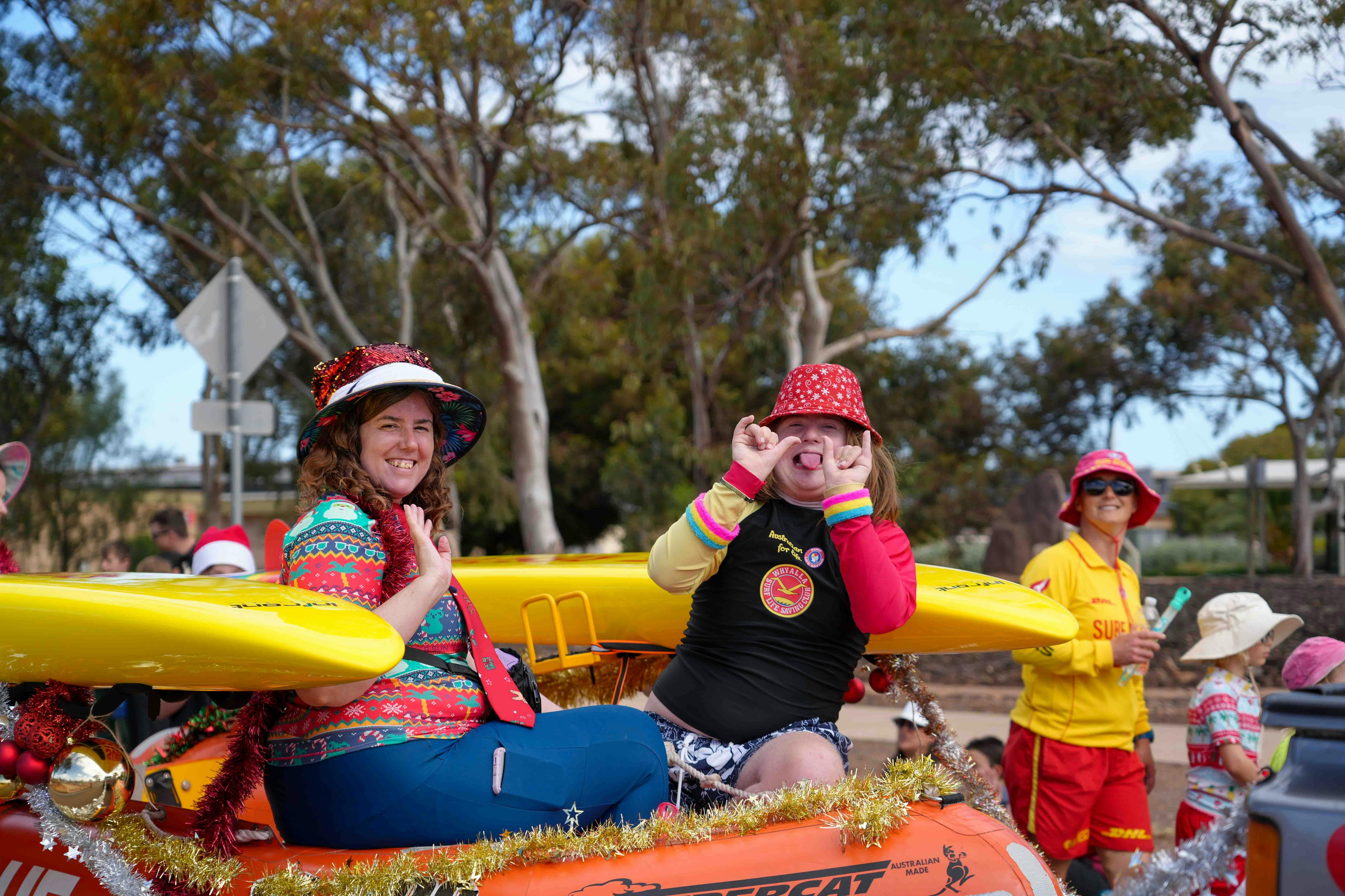 A lady and boy sitting on the surf life save boat wearing Christmas clothes waving and smiling