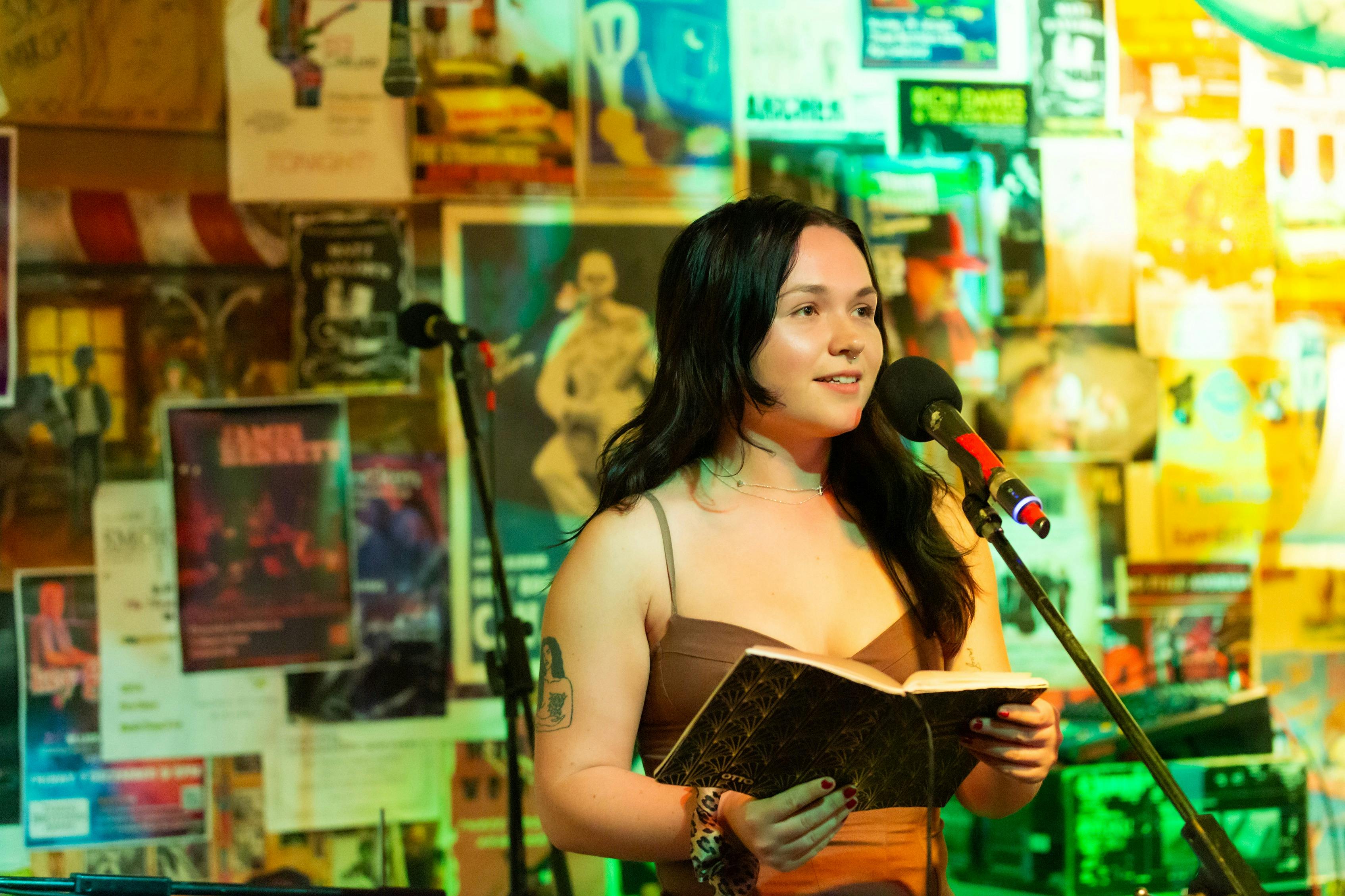 a young woman, on a stage in front of a microphone  with art and posters behind her