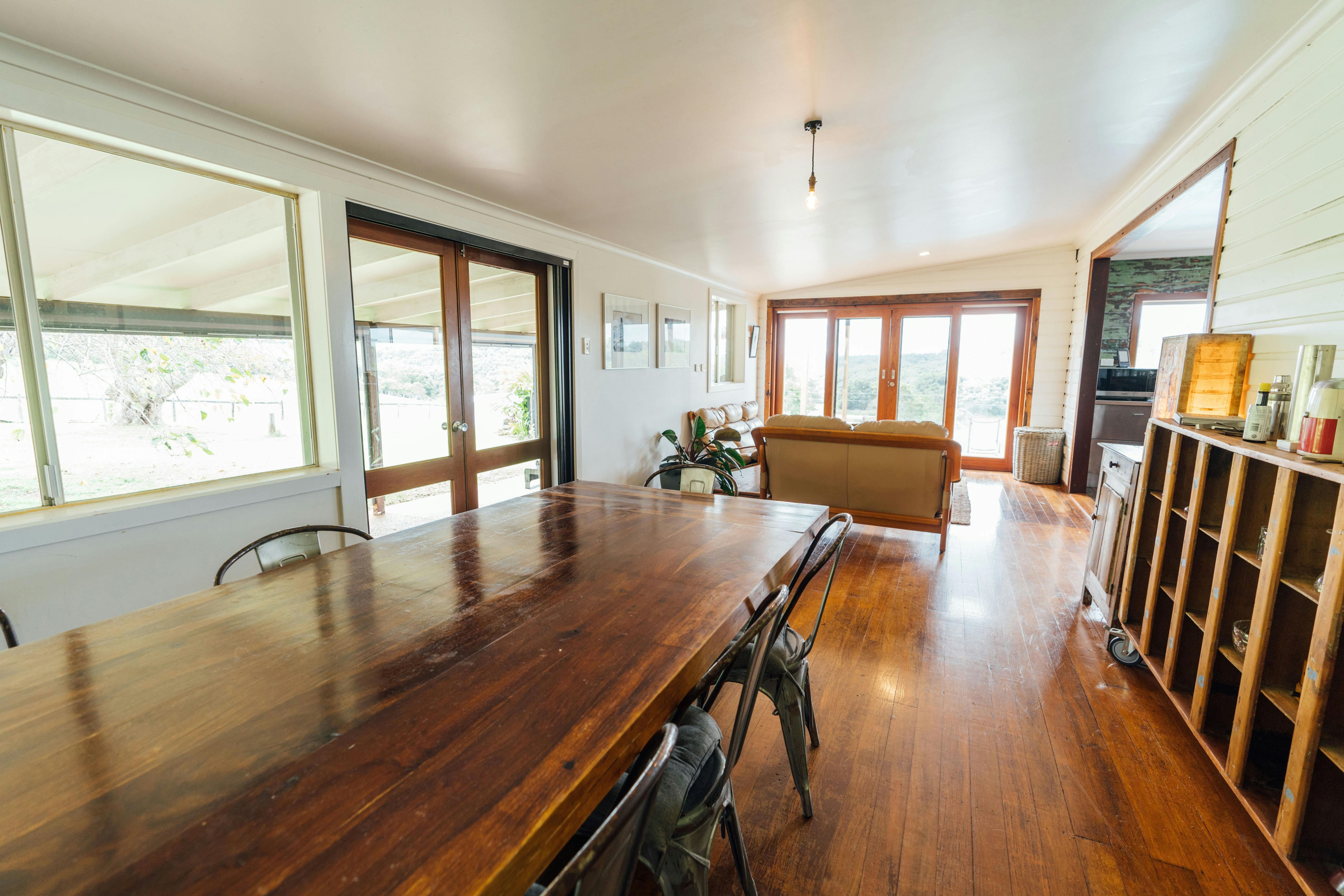 A large timber dining table in a dining room that opens up to a lounge room with leather lounges