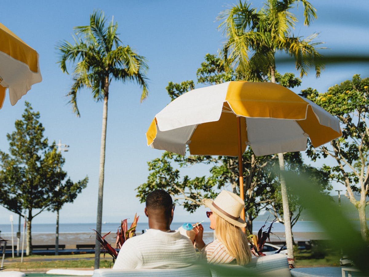 A couple sitting on a sun lounge looking over the esplanade view with cocktails in their hands