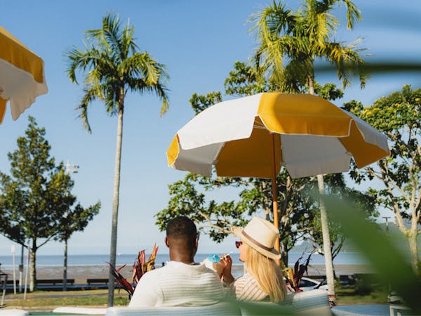 A couple sitting on a sun lounge looking over the esplanade view with cocktails in their hands