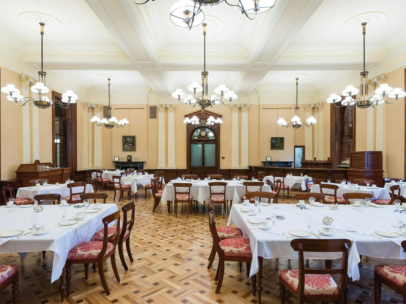 Formal dining room with set tables, lighting, and wooden floors. Formal dining room with set tables, lighting, and wooden floors.